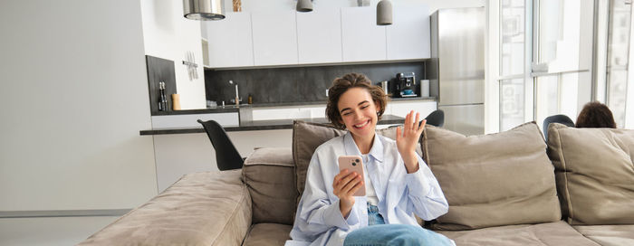 Young woman using mobile phone while sitting on sofa at home