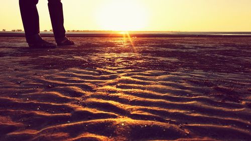 Low section of man standing on beach at sunset