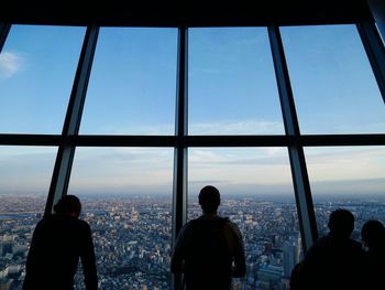 Silhouette people in city against sky seen through window