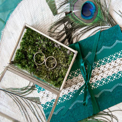 High angle view of wedding ring with gift box and peacock feather on table