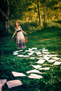 Happy woman with violin standing on sheet music on field