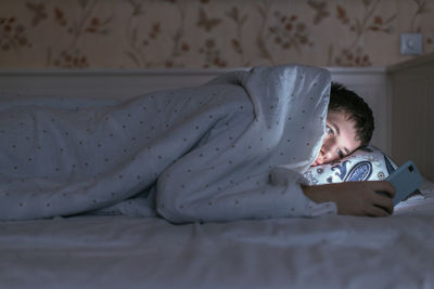 Addicted man under a blanket is surf in web using his smartphone. insomnia and sleeplessness concept