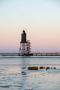 Lighthouse by sea against sky during sunset