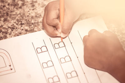 Cropped hands of child writing on book at table