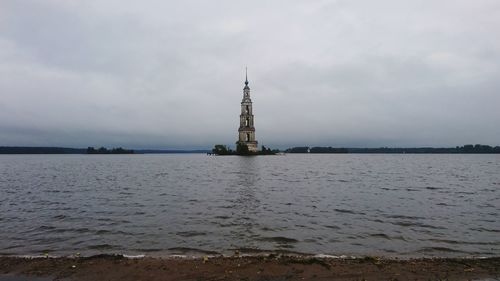 View of tower on sea against cloudy sky