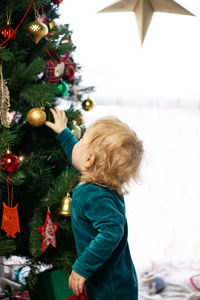 Cute little kid looks at christmas tree decorated with toys and garland. new year and christmas.