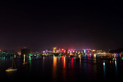 Illuminated city by river against sky at night