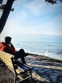 Man sitting on bench by sea against sky