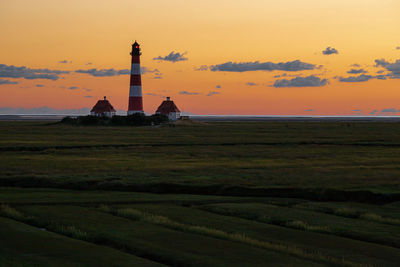 Lighthouse on field against sky during sunset