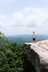 Man standing on rock looking at mountain against sky