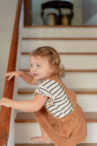 Side view of cute girl climbing on staircase at home