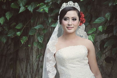 Bride wearing wedding dress and tiara while standing against tree