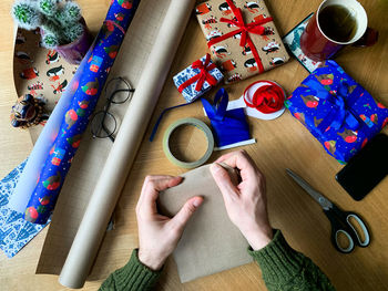 Man wrapping christmas, new year or birthday presents. festive paper and ribbon view from above. diy