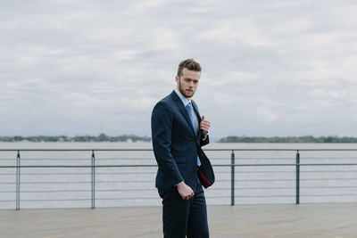 Full length of a young man standing at riverbank against sky