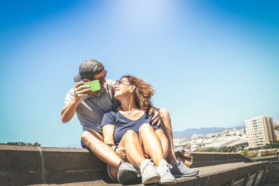 Young couple sitting against clear sky