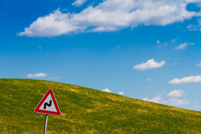 Road sign by field against sky