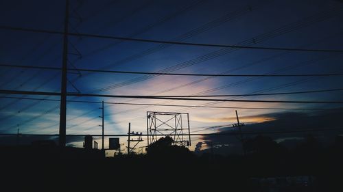 Low angle view of silhouette electricity pylon and building against sky