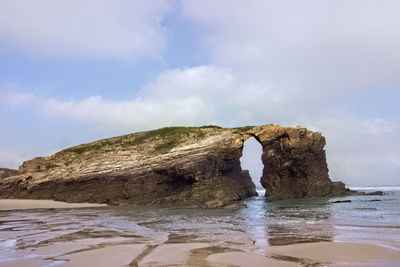 Rock formation on beach against sky