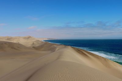 Scenic view of desert by sea against blue sky at sandwich bay