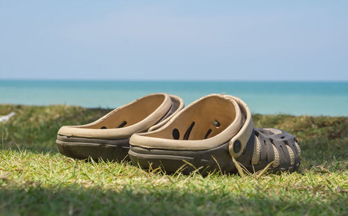 Abandoned shoes on grass by sea against sky