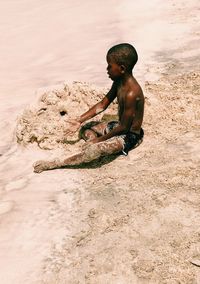 Side view of shirtless boy playing in mud during sunny day