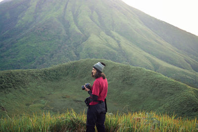 Man holding camera standing against mountain