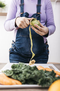 Woman peeling kiwi for preparing fruit smoothie, partial view