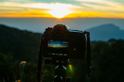 Close-up of camera on landscape against sky during sunset