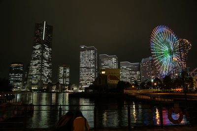 Illuminated city by river against sky at night