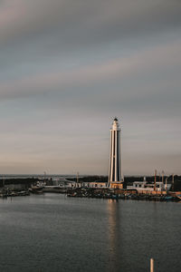 Lighthouse by sea against sky during sunset