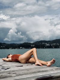 Midsection of shirtless man lying in water against sky