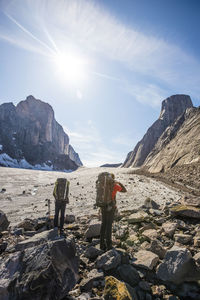 People on rocks by mountain against sky