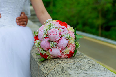 Cropped hands of groom holding bride waist by bouquet on retaining wall