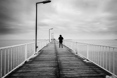 Rear view of man walking on pier over sea against sky