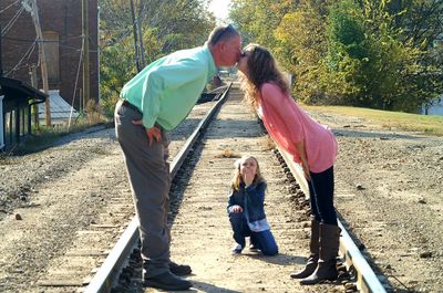 Girl looking at parents kissing on railroad track