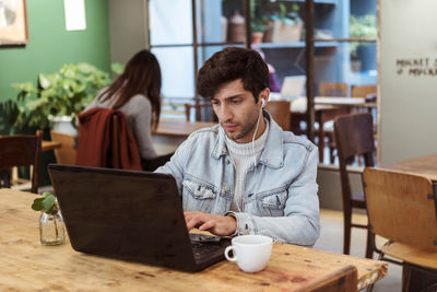 Young man using laptop while having coffee at table in cafe