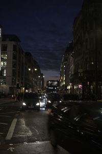 City street by buildings against sky at night