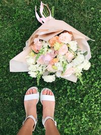 Low section of woman with flower bouquet on grassy field