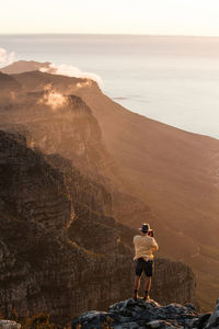 High angle view of man photographing sea on rocky mountains