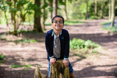 Portrait of boy playing on tree stump at forest