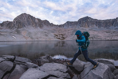 Man standing on rock by lake against sky