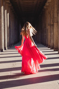 Full length rear view of young woman in pink evening gown walking at colonnade