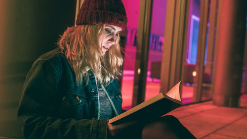 Girl in winter hat reading in front of glass windows