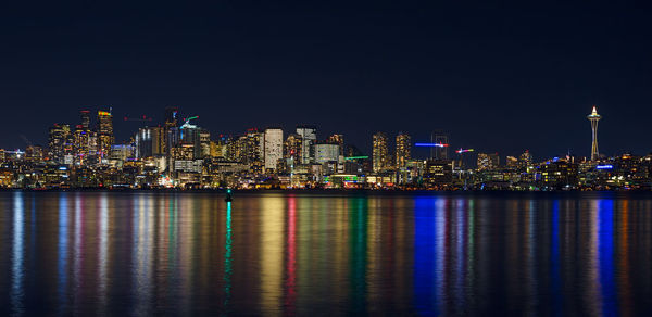 Illuminated buildings by sea against sky at night