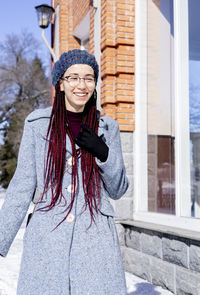 Portrait of young woman standing against window