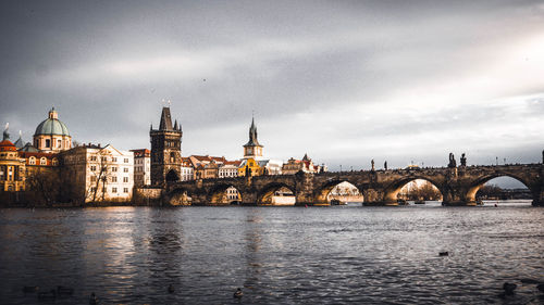 Arch bridge over river by buildings against sky in city