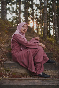 Low angle portrait of young woman sitting on steps in forest