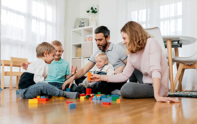 Cheerful parents with children playing with module blocks while playing in light house room