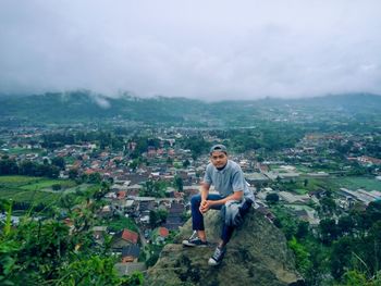 Full length of man sitting on rock against sky