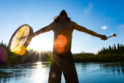 Rear view of woman standing by lake against sky